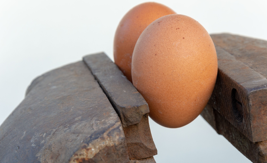 Two brown eggs being squeezed with steel